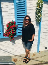 Portrait of young woman standing by flower pot