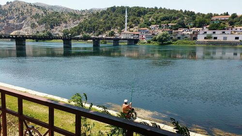 Man fishing at riverbank against mountains