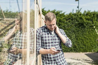 Man using smart phone while leaning on greenhouse