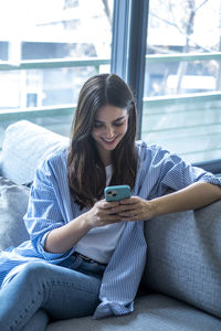 Young woman using mobile phone while sitting on sofa at home