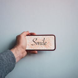 Cropped hand of person holding text against white wall