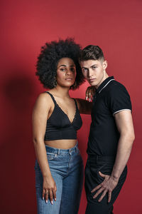 Stylish diverse girlfriend and boyfriend posing in a studio shooting with red background