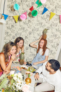 Tilt shot of young multi-ethnic friends enjoying dinner party sitting at apartment