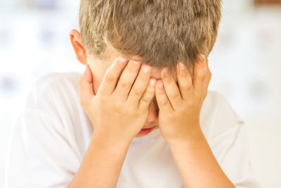 Close-up of depressed boy covering face with hands