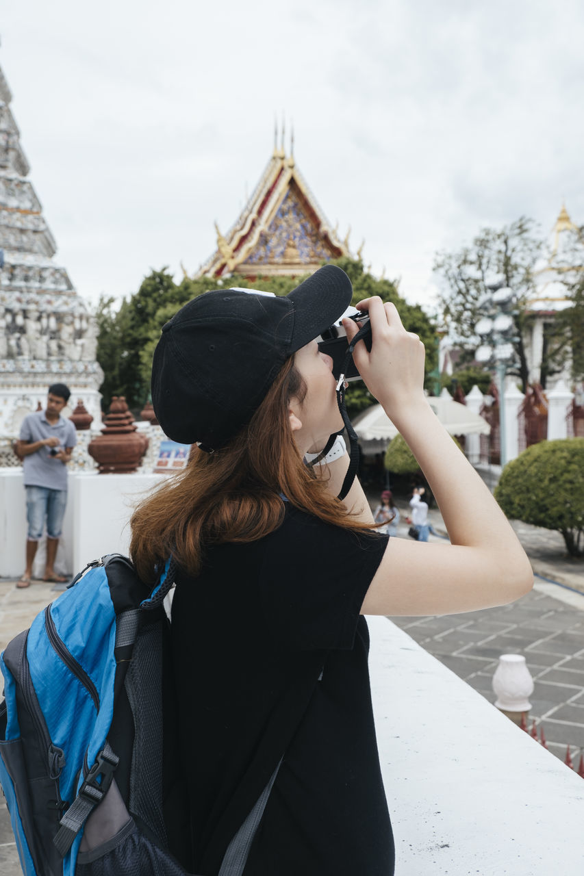 WOMAN WEARING HAT STANDING AGAINST BUILDING