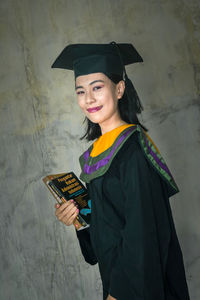 Portrait of smiling young woman standing against wall