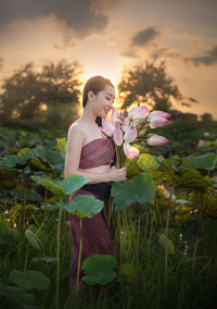 Smiling woman holding water lilies while walking on field