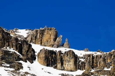 Low angle view of snowcapped mountains against clear blue sky