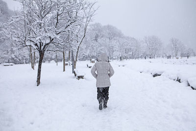 Rear view of man walking on snow covered field