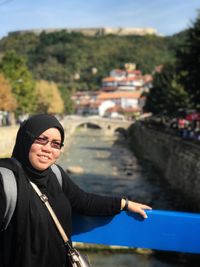 Portrait of smiling woman wearing hijab standing by railing on bridge