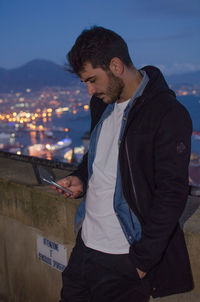Handsome man using mobile phone against illuminated cityscape