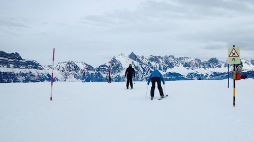 Rear view of people skiing on snowfield against sky