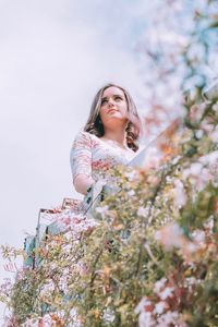 Low angle view of woman by flowering plants against sky