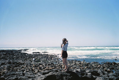 Rear view of young woman standing at seaside against clear sky