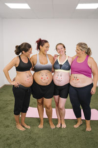 Smiling group of pregnant woman with face drawing on stomach standing at yoga studio