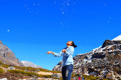 Full length of man standing on rock against blue sky