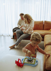 Portrait of happy family sitting on sofa at home and little boy playing with toy on foreground 