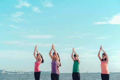 Young friends meditating in prayer position while standing at beach during sunny day