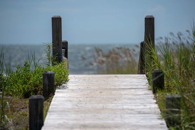 Wooden post on land by sea against sky