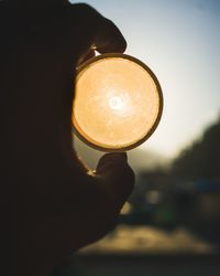 Close-up of hand holding illuminated light bulb against sky during sunset