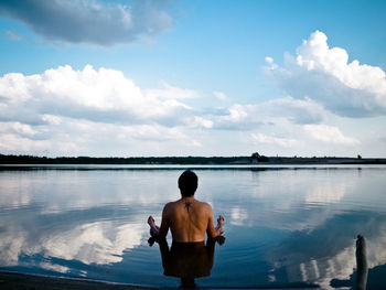 Rear view of man looking at lake against sky