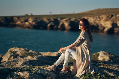 Woman sitting on rock by sea against sky