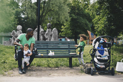 Father holding baby boy while looking at son in public park