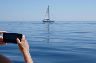 Man photographing sailboat in sea against sky