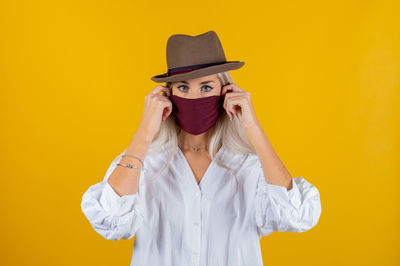 Portrait of young woman wearing mask and hat against yellow background