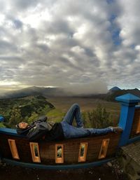 Man sitting on land against cloudy sky