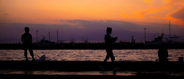 Silhouette people on beach against sky during sunset