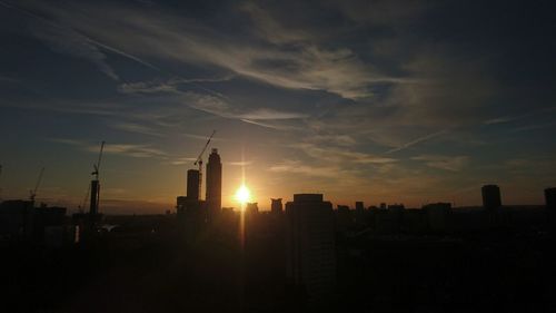 Silhouette of city against cloudy sky during sunset