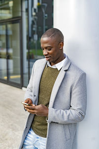 Businessman using smart phone leaning on column