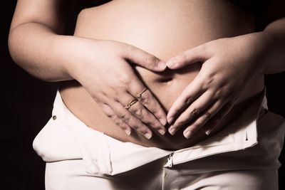 Midsection of woman touching hair over black background