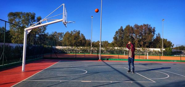 Man playing with basketball court against sky