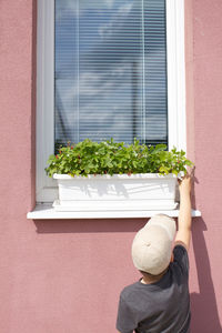 Man standing by potted plant against window