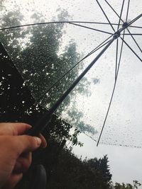 Close-up of hand holding wet smart phone against sky