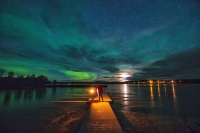 Rear view of person standing on pier over lake at night