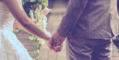 Midsection of bride and bridegroom holding hands during wedding ceremony