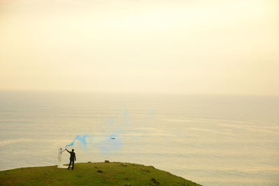 Couple with distress flare standing at beach against sky