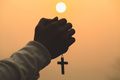 Both hands grasped the cross to pray to god. while the sun is setting or rising.