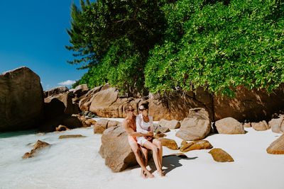 Smiling couple sitting on rock at beach