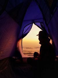 Silhouette man sitting in tent during sunset