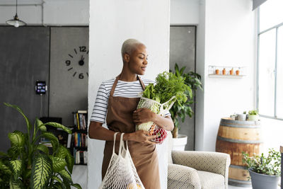 Pretty woman in apron carrying net with fresh vegetables