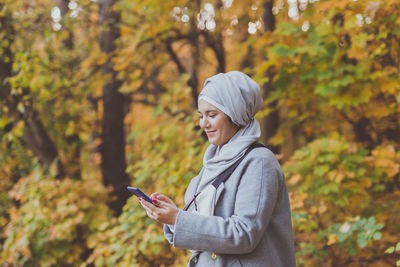 Young man using smart phone while standing on tree