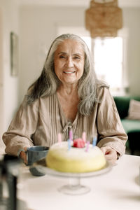 Portrait of smiling senior woman with birthday cake on table at home