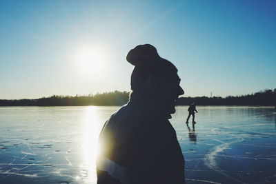 Silhouette senior man standing by lake against clear blue sky