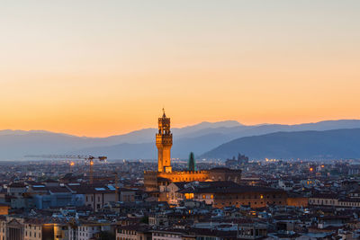 Illuminated buildings in city against sky during sunset