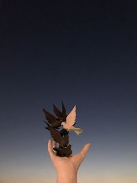 Cropped hand holding artificial birds against clear sky