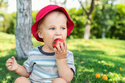 Close-up of cute baby boy eating apple sitting on grass